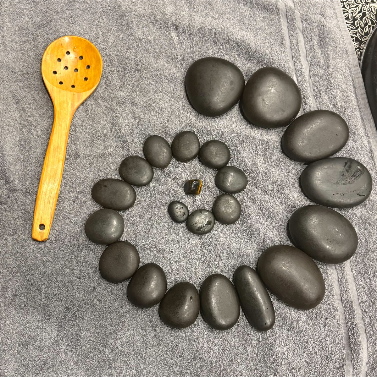 Basalt hot stones laid out in a spiral on a towel with a wooden ladle